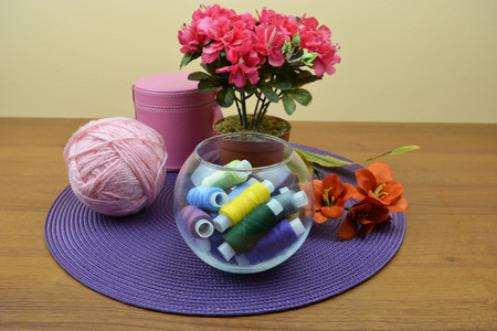 Glass bowl with coils of threads. A ball of pink yarn. Red flowers on violet background. Beautiful combination of threads, glass cup, flowersの写真素材