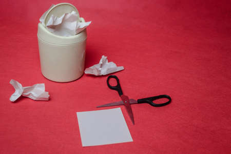 Light trash bin on a red background. Closeup of crumpled sheets of paper and scissors. The concept...