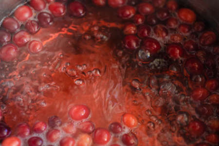 Homemade berries compote preparation. Fresh juice of berries boiling in a pot. Organic cranberries autumn and winter beverage. European cuisine stewed fruit cooking in a pan. Red drink close-up.の写真素材