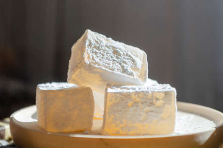 Delicious white traditional bulgarian turkish delight on wooden dish sprinkled with icing sugar like snow. Oriental pieces of sweets for tea close-up. Winter Christmas dessert in the bright sunshine.の写真素材