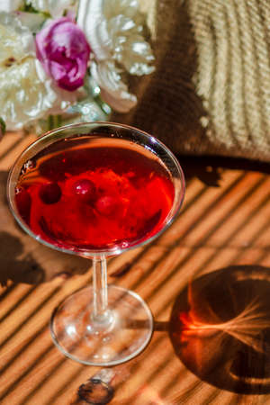 Solemn rustic still life with glass of red drink with autumn berries and white flowers on a wooden table and textile in the diagonal striped shadow of the blinds in bright sunny day. Rich colors.の写真素材