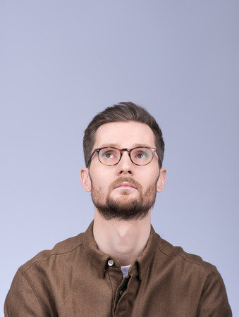 Stylish modern guy thinks about something, lifting his head up. Neutral facial expression. The beard and glasses. Neutral grey backgroundの写真素材