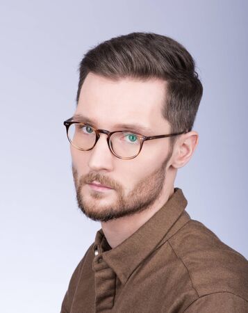 Fashion portrait of stylish young man in brown shirt. The beard and glasses. A modern way. Neutral grey backgroundの写真素材