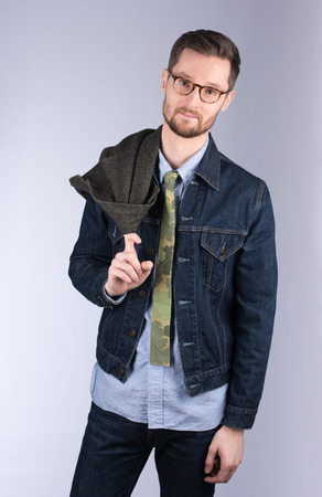 Vertical portrait of a handsome young man in stylish modern clothes. Man holding coat at shoulder. Glasses and beard. Neutral grey backgroundの写真素材