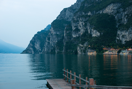 Twilight. View of mountain lake with pier. The rocky shore. Silhouettes of housesの写真素材