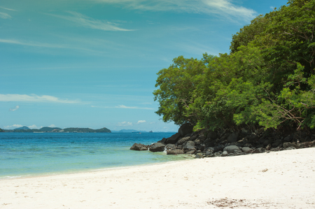 Beautiful tropical beach with sea view, black rocks with green trees. The nature of the background. Toned photoの写真素材