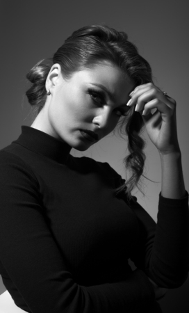 Portrait of beautiful woman with sexy look is sitting on chair on grey background. The girl holds a hand over his head in frontの写真素材