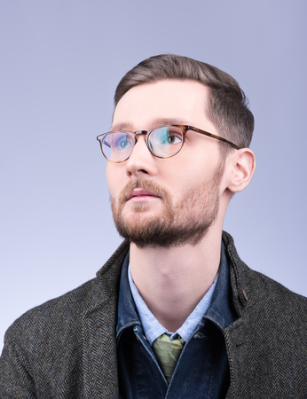 Men's style. Vertical portrait of a young man with a beard and neat hair. Denim clothing and coats. Neutral grey backgroundの写真素材