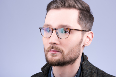 Stylish men's glasses. Closeup portrait of young man with beard and mustache. Neutral grey backgroundの写真素材
