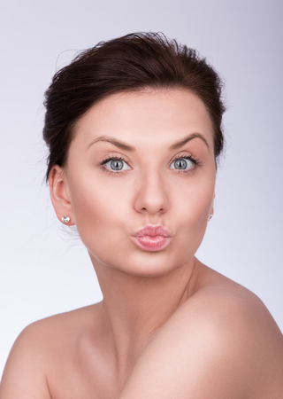 Beautiful young woman folded her lips for a kiss. Closeup portrait on a neutral grey backgroundの写真素材