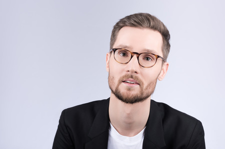 Portrait of stylish young man with glasses. Black jacket and white t-shirt. Beard and mustache. Neutral grey backgroundの写真素材