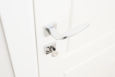 Modern door handle and escutcheon for lock with key. Chrome interior details in close-up. White door and light grey wallの写真素材