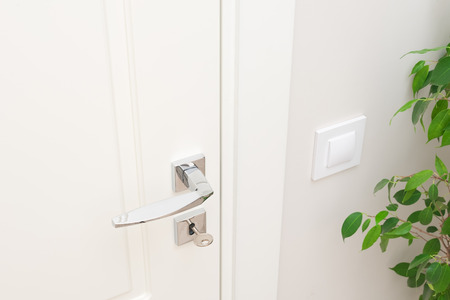 Modern metal door handle and escutcheon for lock with key. Close-up elements of the interior. White door and white wall with switchの写真素材