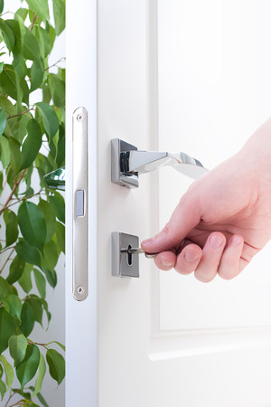 Door lock closeup of a male hand with a key. Modern chrome door fittingsの写真素材