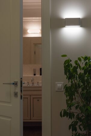 Wall LED lamps in the interior. Open white door to the bath. Comparison of led and halogen lightの写真素材