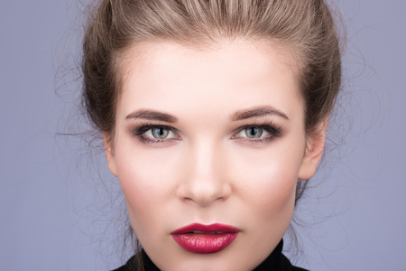Portrait closeup of face of beautiful young woman with expressive eyes. Makeup and red lipstick on her lips. The hair is collected. Neutral grey backgroundの写真素材