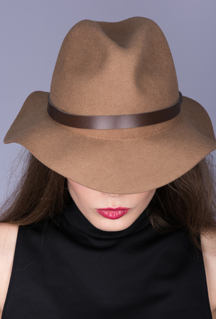 Vertical portrait of a woman in a brown hat and black clothing with her hair. Hidden face visible only lips in red lipstick. Neutral grey backgroundの写真素材