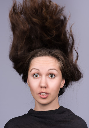Vertical portrait of a young attractive woman with flying hair. Hair flies in the wind. The hair on his head. The woman surprised. Neutral grey backgroundの写真素材