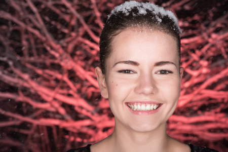 Closeup portrait of a young woman in the night snowy forest. It's snowing. Reddish backgroundの写真素材