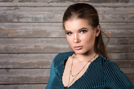 Horizontal portrait of a beautiful young woman in a green dress. Professional Nude makeup. Perfect clean skin. Dark gray background with horizontal stripesの写真素材