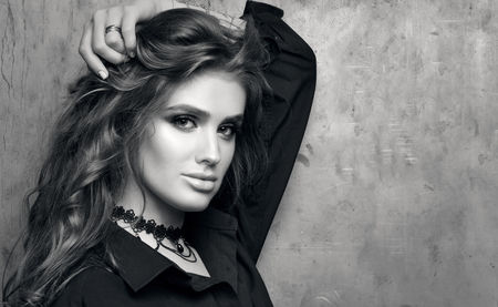 Black and white closeup portrait of young beautiful woman in black shirt posing in front of a metal wall. Luxurious healthy hair and professional makeup. Black choker. Free space for photosの写真素材