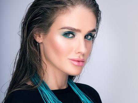 Beauty closeup portrait of beautiful young woman with wet hair and professional makeup. Necklace on her neck. Stylish in appearance. A neutral grey backgroundの写真素材