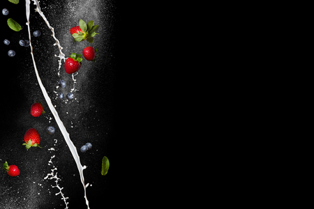 Berry mix. Fresh ripe strawberries and blueberries in flight on a black background. Spiral streams of milk. Free spaceの写真素材