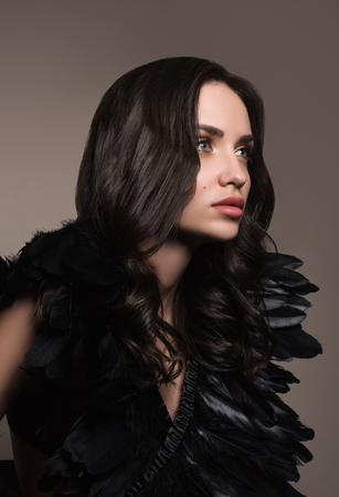 Vertical fashion portrait of young beautiful woman in black. Black hair and black feathers. Professional make-up. A neutral backgroundの写真素材