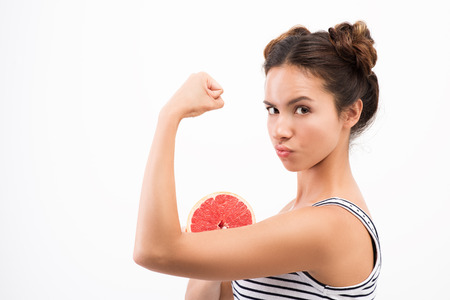 The strength of the fruit. Young pretty woman with half a grapefruit attached to my hand. White backgroundの写真素材