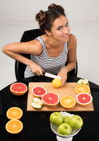 Healthy eating and freshness. The pretty young woman cut citrus fruit sitting at the tableの写真素材