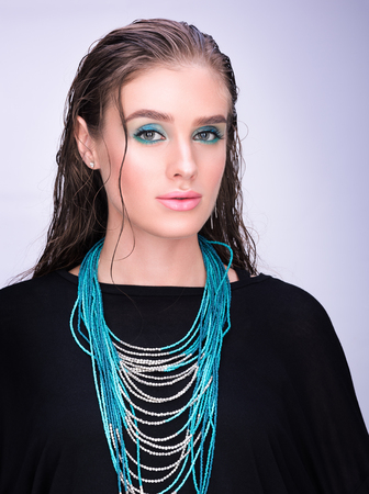 Vertical portrait of a young woman in black. Wet hair and professional makeup. Sensual look. Turquoise necklaceの写真素材