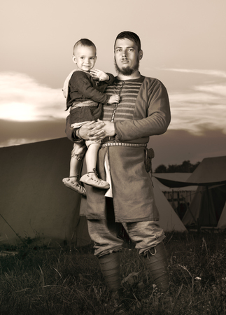 Tinted antique portrait of a slavic man with a baby in historical costume. The image of a man from the past. Vintage clothing. A father and his son. The sunset in the backgroundの写真素材