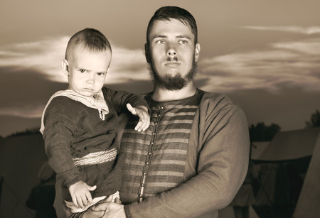 Toned portrait of a Slavic man with a baby in historical costume. The image of a man from the past. Vintage clothing. A father and his son. The sunset in the backgroundの写真素材