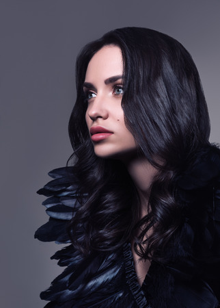 Fashion portrait of young beautiful woman in black. Black hair and black feathers. Professional make-up. A neutral backgroundの写真素材