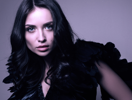 Fashion closeup portrait in cool tones. Young beautiful woman in black. Feathered dress, makeup and hairstyleの写真素材