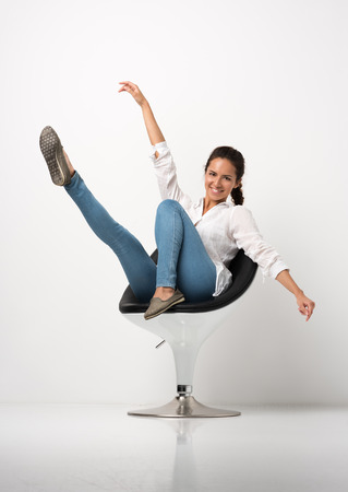 Vertical portrait of a young cheerful woman posing in modern armchair. Everyday appearance. The white wall in the backgroundの写真素材