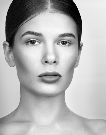 Black and white beauty portrait closeup. Beautiful young woman with bright professional make-up. The hair is collected. Perfect clean skin. A neutral grey backgroundの写真素材