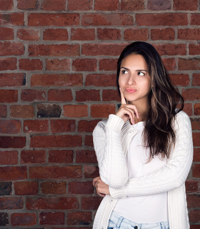 Vertical portrait of an attractive young woman. To think about something or to choose something. Brick wall with free space in the backgroundの写真素材