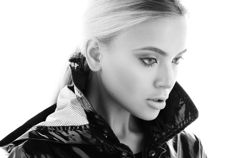Black and white beauty portrait of beautiful young woman in a black glossy coat. The gaze is directed downward. professional makeup, hair collected. Isolated on bright white backgroundの写真素材