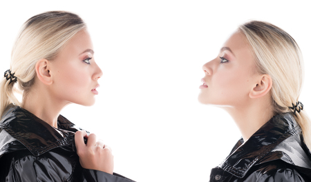 Comparison and envy. Portrait of two young women-twins looking at each other. Glossy black Cape, hair collected, professional makeup and clean skinの写真素材