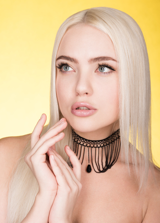 Beauty portrait of beautiful young woman on a yellow background. Choker on the neck. Blonde with straight hair and light makeupの写真素材