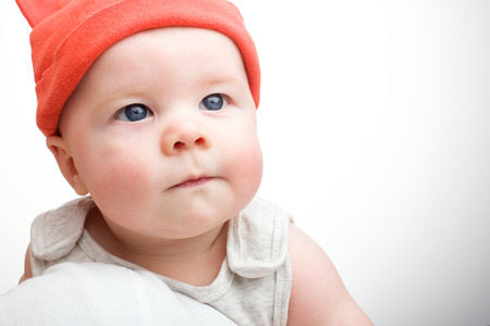 Closeup of the face of the baby in the hat on a light background. Handsome little boy with blue eyesの写真素材