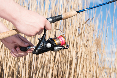 Spinning in the hands of the fisherman. Closeup of fishing gear and dry tall grass in the background.の写真素材