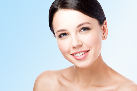 Closeup beauty portrait of young woman with beautiful smile. Neutral blue background with free spaceの写真素材