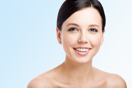 Smiling young woman on light background. Perfect clean skin. Kind face. Close-up beauty portraitの写真素材