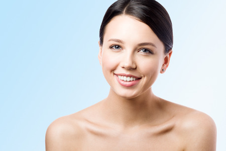 Close-up portrait of a young woman with a smile on her face. Perfect skin. Blue background with free spaceの写真素材