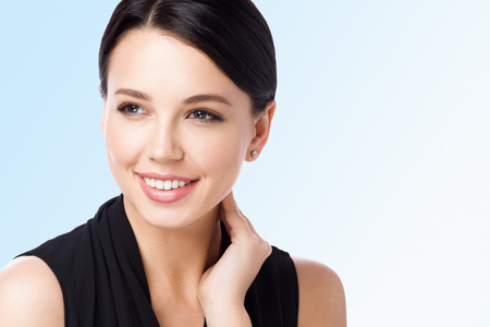 Closeup of portrait of beautiful woman touching neck. Perfect clean skin and smile. Isolated on blue backgroundの写真素材