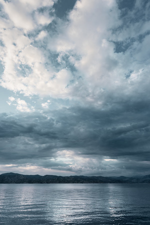 Epic seascape. Heavy clouds and mountains on the horizon, the sea in the foregroundの写真素材