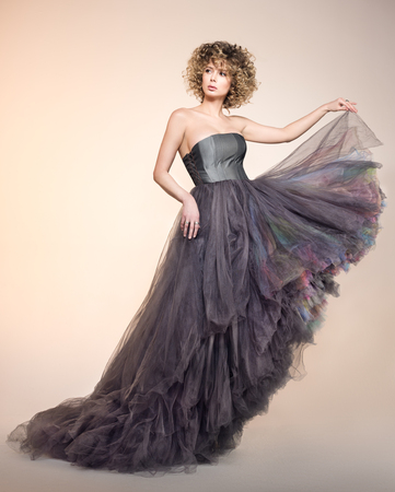 Fashion portrait of beautiful young woman in a lush grey dress. Curly hair. Neutral beige backgroundの写真素材
