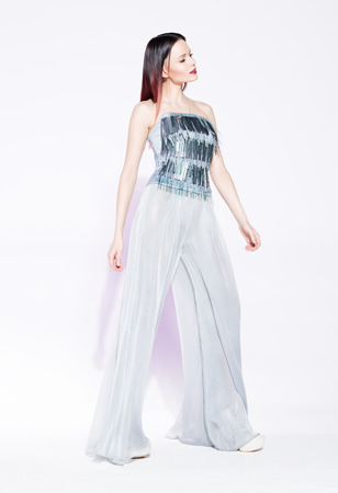 Fashion model posing in a silver suit with wide pants on white background. Stylish, modern young woman in fashionable clothingの写真素材